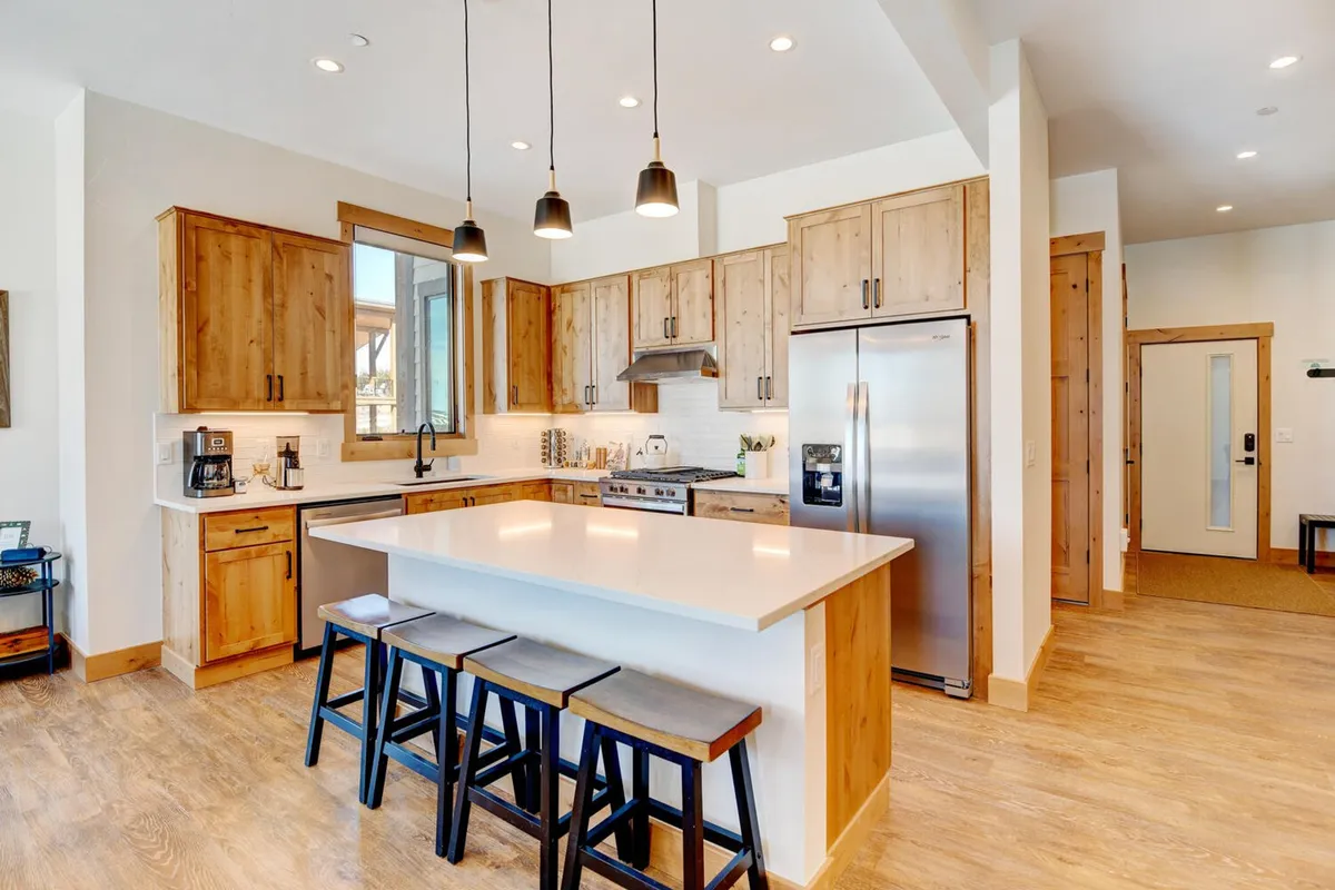 This image showcases the heart of the kitchen with a central island, wooden cabinets adding warmth, and gleaming stainless steel appliances. The island provides ample bar seating, inviting both cooking and gathering. The atmosphere exudes coziness and a welcoming vibe, perfect for communal meals and socializing.