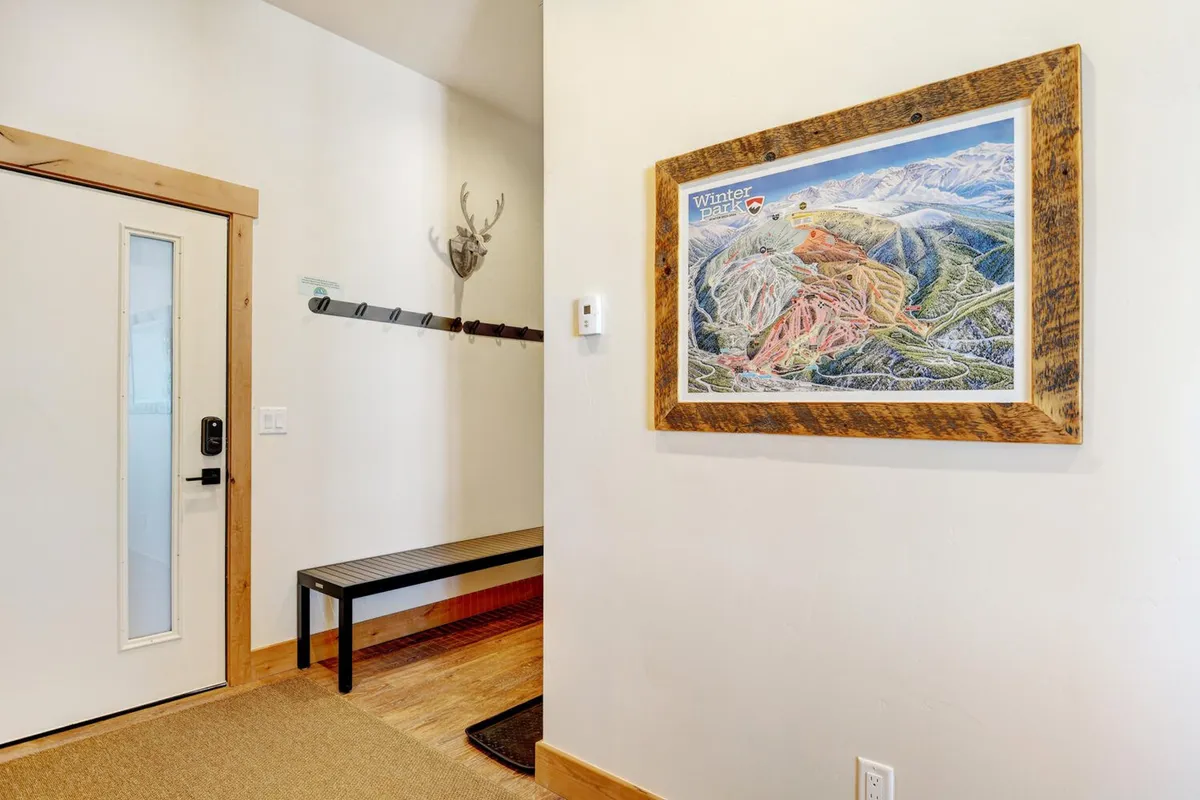 A cozy and inviting entryway featuring a framed map of Winter Park, a wooden bench, coat hooks, and rustic antler decor. The area is designed for gearing up before heading out or returning from outdoor adventures.