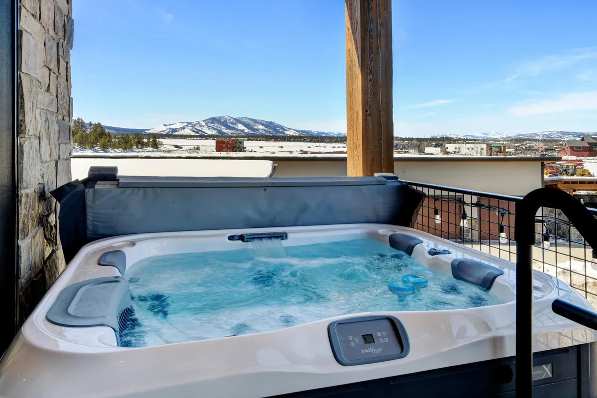 This image showcases a private hot tub set on a balcony with a panoramic mountain view and a clear sky overhead. The tranquil setting suggests the perfect place for relaxing soaks after outdoor adventures, with space for friends or family to gather. The sunset lighting further amplifies the inviting, restful mood.