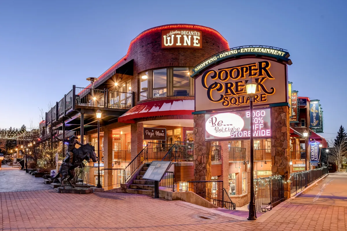 The vibrant Cooper Creek Square entrance, highlighted by signs for dining, wine shops, and a sculpture of a horse. The scene suggests a lively social atmosphere with options for shopping, dining, and entertainment—all within walking distance.