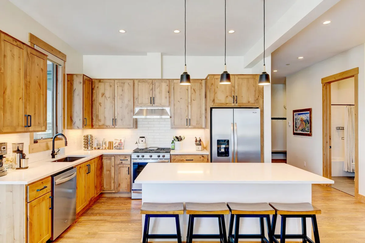 This kitchen features a generous island with seating, pendant lights overhead, rich wood cabinets, and a suite of stainless steel appliances. The setup is ideal for both cooking and entertaining, with ample counter space and a layout that encourages interaction.