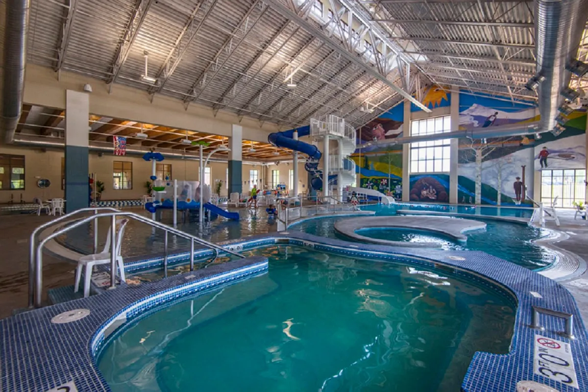 An inviting, colorful indoor pool area with a large water slide and a cheerful mural. The scene shows families and children enjoying the swimming pool—an unmistakable nod to the Grand Park Rec Center’s offerings just down the street.