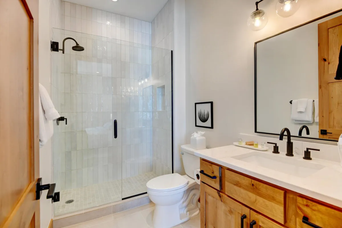 A spa-inspired bathroom featuring a glass shower enclosure, a stylish wooden vanity with a large mirror, and sleek black fixtures. The bathroom is bright, modern, and welcoming, ideal for unwinding after a day of adventure.