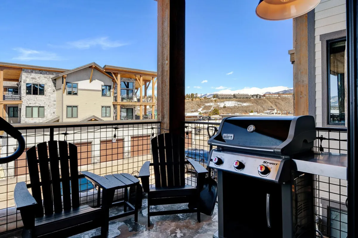 The balcony is depicted with a BBQ grill and several Adirondack chairs arranged to capture the mountain view. The scene exudes a casual, sociable vibe, hinting at alfresco meals and friendly gatherings against a stunning natural backdrop.
