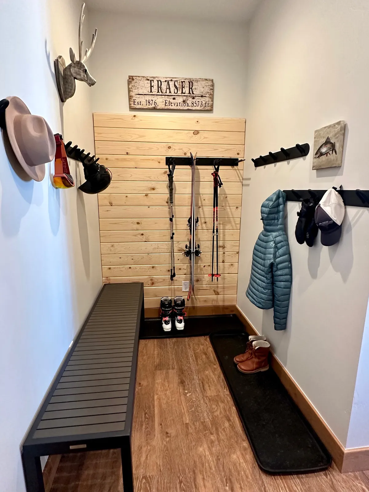 A practical and inviting ski locker area with wooden wall paneling, ski equipment, sturdy coat hooks, and a comfortable bench—perfect for organizing gear and preparing for outdoor activities.