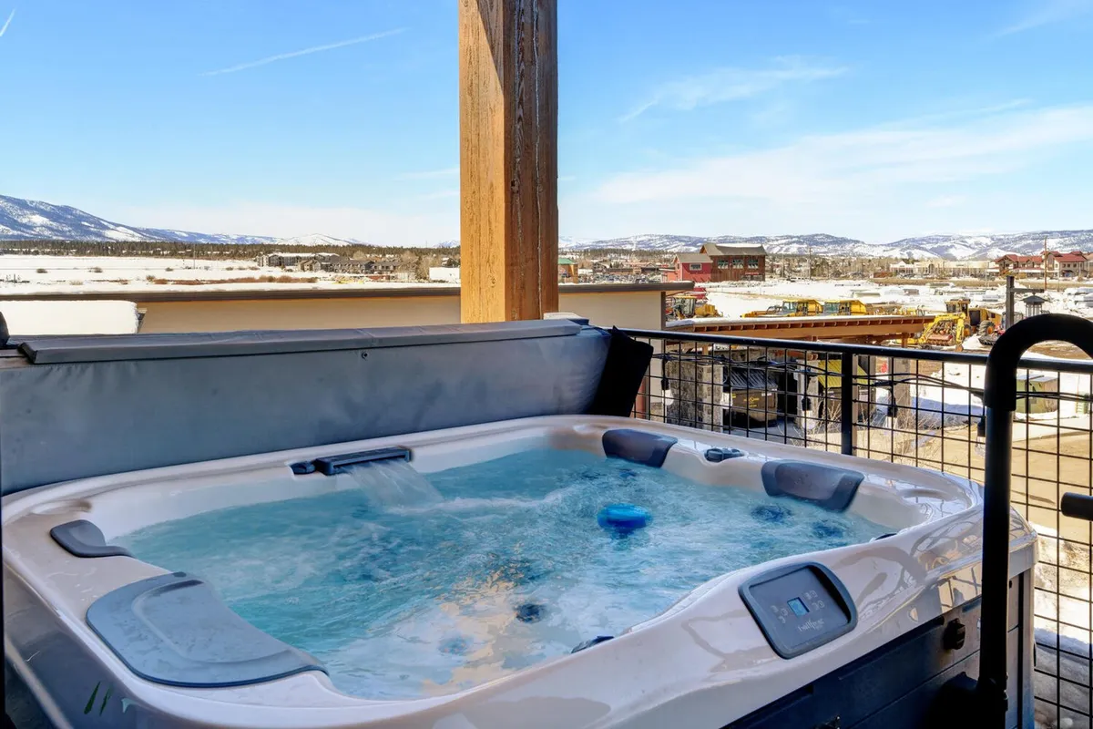 A tranquil outdoor hot tub with clear views of the mountains under a bright sky, inviting guests to unwind after a day of adventure. The scene is peaceful, promising relaxation and scenic beauty.